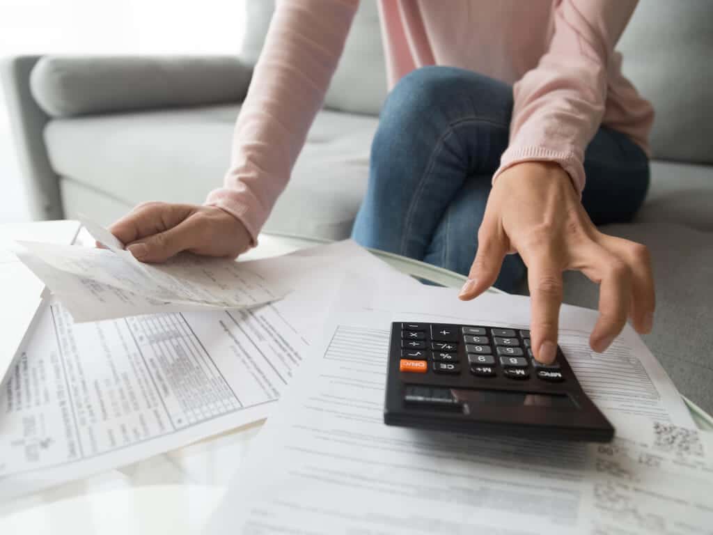 documents strewn across a coffee table as a woman calculates bills