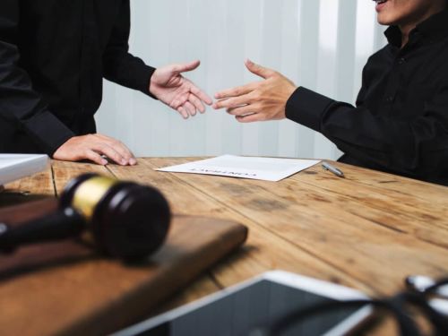 two people in front of a table shaking hands over a legal document