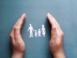 paper cutout of a family in between hands on a blue background